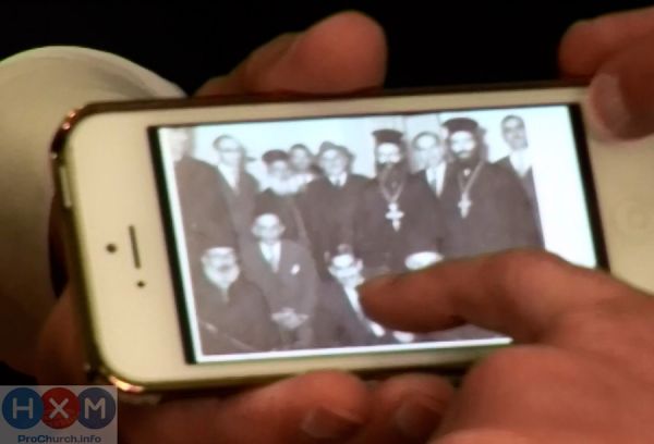 Пастор Бенни Хинн показывает на телефон фото своего отца в окружении православных священников